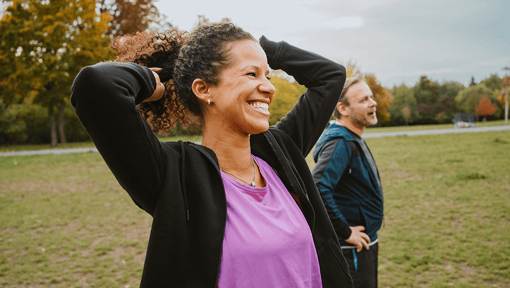 a woman and man standing outside. the woman is putting her hair up and smiling.