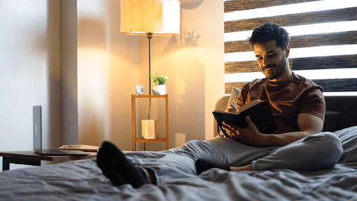 A man sitting up in bed with a book, practicing a mindful moment.