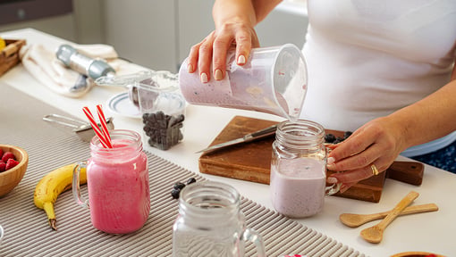 Preparing homemade berry smoothies in glass jars with fresh bananas and blueberries on a kitchen countertop.