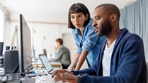 Two coworkers collaborating while looking at a laptop screen.