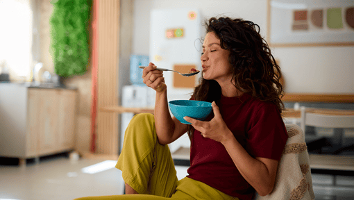 A woman seated indoors, focusing on a meal as an example of mindfulness during everyday activities.