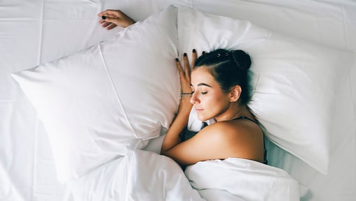 man sleeping in a bed surrounded by white pillows and bedding.