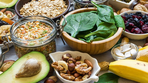 Variety of nutrient-rich foods including spinach, avocado, nuts, oats, dried berries, and legumes arranged on a table.