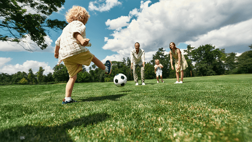 Family fitness activity outdoors as a child kicks a soccer ball across a grassy field while other family members participate in the game.