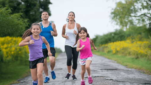Two adults and two children jogging together on an outdoor trail, demonstrating family fitness, physical activity, and healthy lifestyle habits.