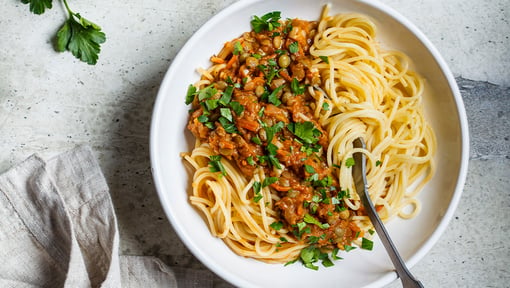 Bowl of spaghetti topped with a savory tomato-based sauce and fresh herbs.