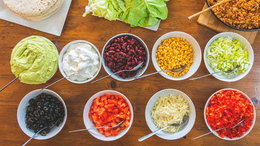 Build-your-own meal ingredients arranged in bowls, including vegetables, beans, corn, cheese, and toppings.