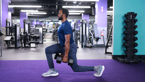 A man performing a weighted lunge exercise in a gym to build lower-body strength and improve mobility.